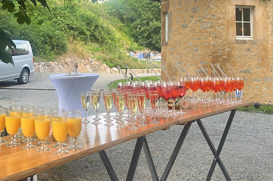 Ein Tisch mit bunten Getränken im Freien, neben einem steinernen Gebäude.