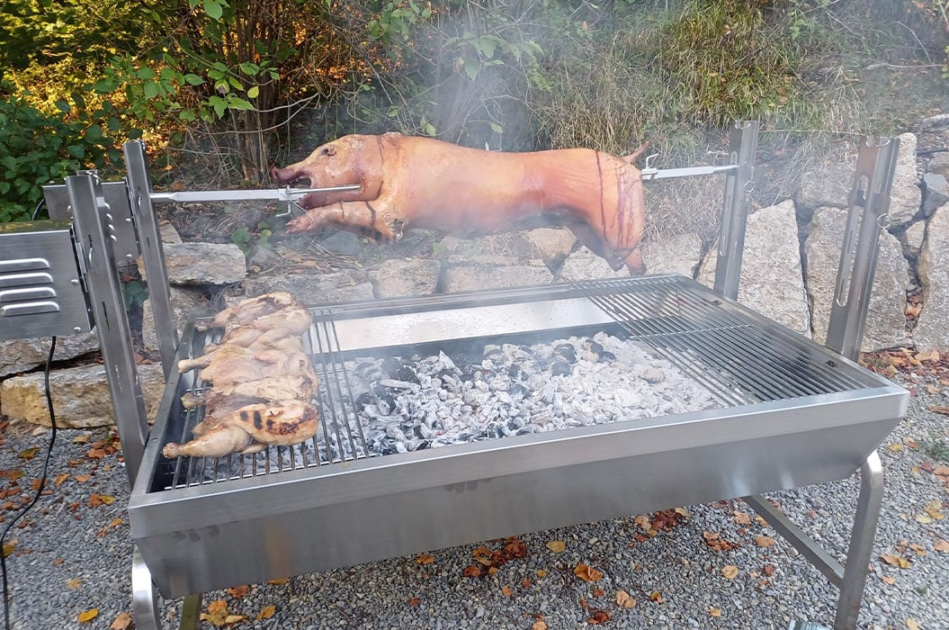 Ein Spanferkel und gegrilltes Hähnchen auf einem Grill im Freien, umgeben von Rauch.